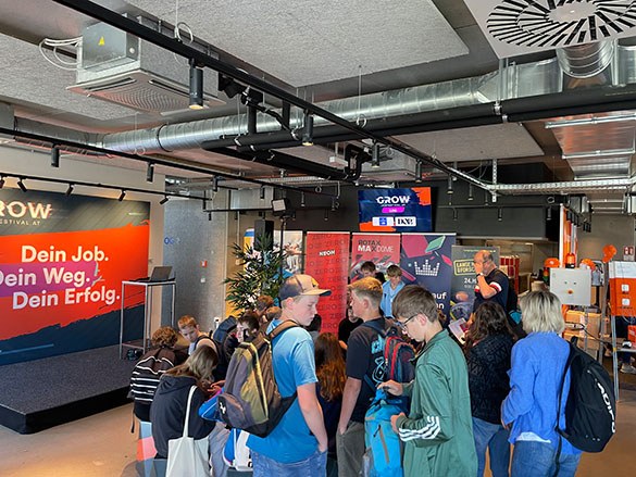 meinkarrierestart.at Eine Gruppe von Menschen versammelt sich bei einer Karriereveranstaltung in einem geschlossenen Raum mit Informationsständen, Bannern und einer kleinen Bühne im Hintergrund.